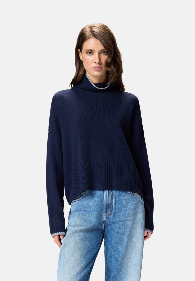 Sweater court bleu marine avec un col haut et un ourlet côtelé, doté d'une texture douce. Associé à un jean en denim bleu clair.