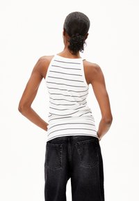 Weißes Tanktop mit schwarzen horizontalen Streifen, geripptem Material und hohem Kragen, kombiniert mit lockeren schwarzen Jeans mit Gesäßtaschen.