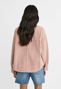 Giacca di jeans rosa chiaro con una vestibilità rilassata, caratterizzata da una cucitura sul retro e due tasche laterali, abbinata a shorts di jeans strappati.