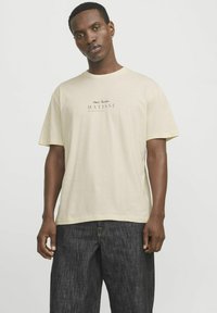 Cremfarbener T-Shirt mit kurzen Ärmeln aus weichem Stoff, mit schwarzem Drucktext "Henri Matisse" und "Blue Wine Style Lab" mittig auf der Brust.