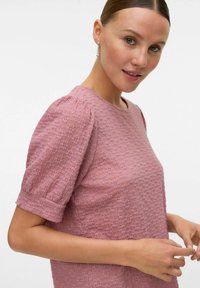 Roze textuur top met korte pofmouwen, ronde halslijn en subtiele bloemmotieven. Gladde stof met een iets gestructureerd ontwerp.