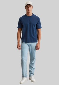 Granatowa koszulka bawełniana z okrągłym dekoltem, połączona z jasnoniebieskimi dżinsami i białymi trampkami. Prosty, casualowy styl.