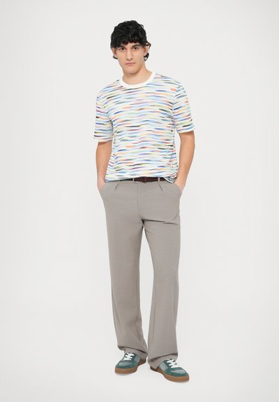 Majica s kratkimi rokavi z večbarvnimi črtami in belim ovratnikom, združena s svetlo sivimi hlačami in zelenimi supergami z belimi vezalkami.