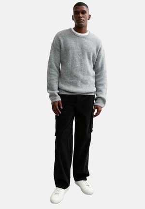 Szary sweter dzianinowy z okrągłym dekoltem, zestawiony z czarnymi spodniami cargo. Model nosi białe sneakersy. Materiał wydaje się strukturalny i ciepły.