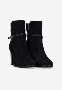 Botines de ante negro con un acabado texturizado, una silueta elegante, cierre lateral y una correa negra mate con un accesorio de hebilla dorada.