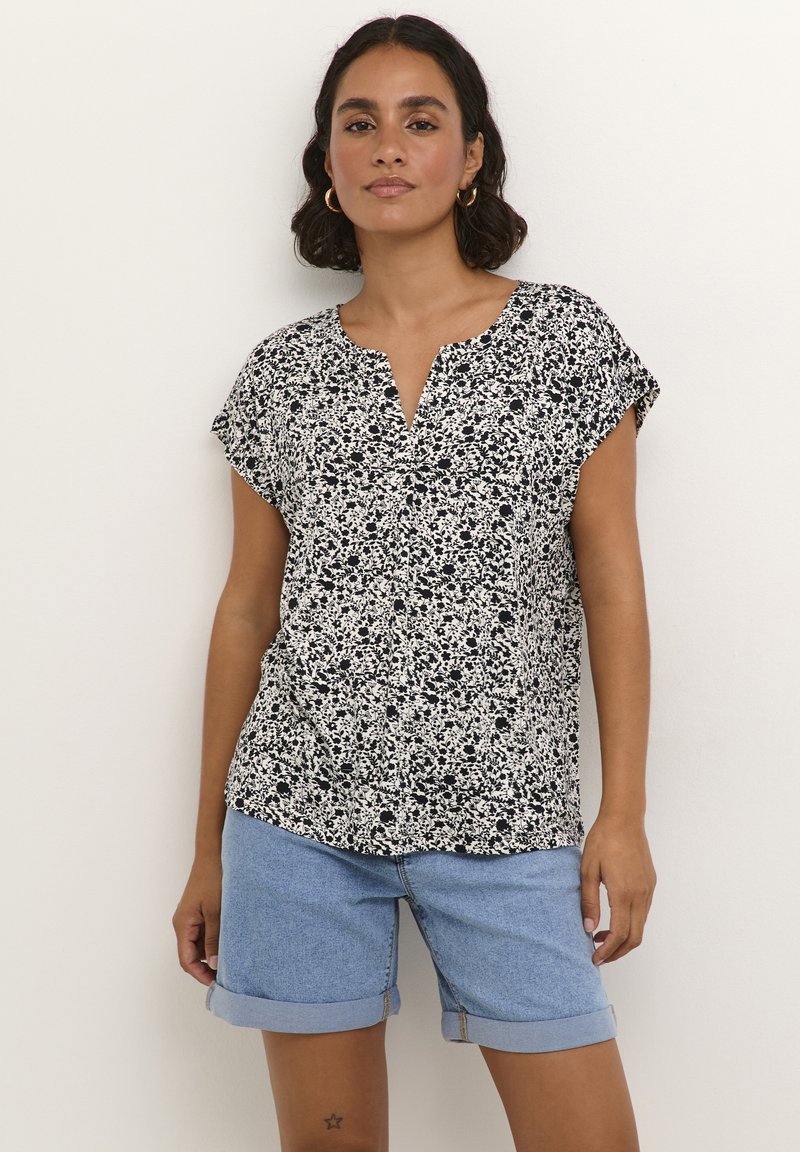 Blouse florale noir et blanc à manches courtes et décolleté en V, associée à un short en denim bleu clair. Tissu doux et coupe décontractée.