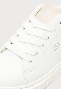 Λευκό αθλητικό παπούτσι Tommy Hilfiger με λευκά κορδόνια, μπεζ επενδεδυμένη γλώσσα και ελάχιστο λογότυπο στο πλάι κοντά στη ραφή.