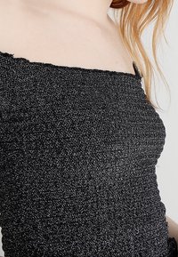 Czarny, bezramkowy top wykonany z żebrowanej tkaniny o lśniącej fakturze. Posiada prosty dekolt i dopasowany krój.