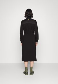 Black long-sleeve dress with a fitted waist, featuring a high collar, and a solid texture. Paired with green ankle boots.