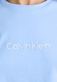 Světle modré tričko s vyšitým nápisem "Calvin Klein" v bílé barvě, představující minimalistický design.