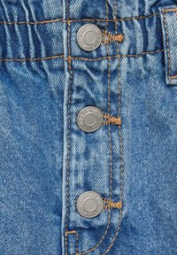 Denim tkanina v svetlo modri barvi s štirimi srebrnimi kovinskimi gumbi in kontrastnim svetlo rjavim šivom na sprednji strani. Teksturo površine dopolnjujejo blagi učinki obrabe.