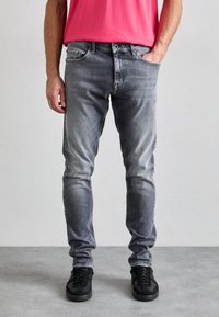 Slim-fit šedé džíny s vybledlým efektem, pět kapes, zapínání na knoflíky a jemné detaily prošití, doplněné černými teniskami.