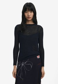 Navy, long-sleeve knit sweater with a sheer texture and round neckline, layered over a patterned skirt featuring floral designs.