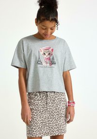 Grå t-shirt med kort ärm och en kattgrafik, som är tillsammans med en skär leopardmönstrad kjol. Noterbara armband på handleden.