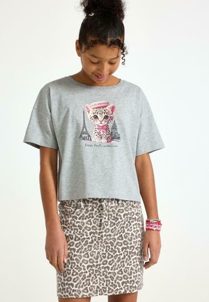 Grå kortærmet t-shirt med kattekunst, parret med en tan leopardmønstret nederdel. Bemærkelsesværdige armbåndsaccenter på håndleddet.