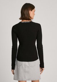 Svart ribbad tröja med lång ärm och figurnära design, med en vit "Pepe Jeans"-logotyp vid bakre halsringning.