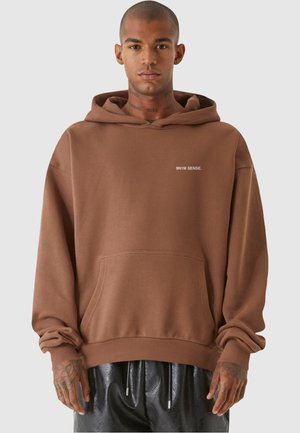 Brun hætte sweatshirt lavet af blødt stof, med en lomme foran og hvid tekstlogo. Løs pasform med ribbede manchetter og kant.