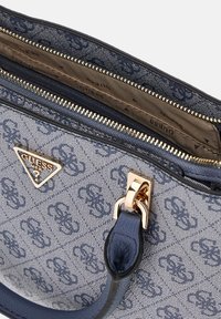 Sac à main bleu à motifs avec un tissu texturé, des accessoires dorés et une étiquette de logo triangulaire. Il présente une fermeture éclair et une bandoulière en cuir.
