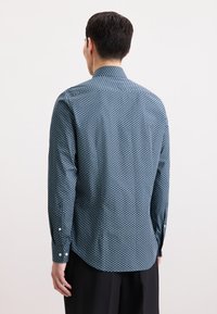 Camicia blu con motivo geometrico, maniche lunghe, polsini con bottone e un leggero arco all'orlo. Tessuto dal tocco liscio.