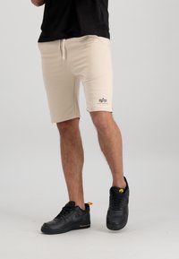 Bež kratke atletske hlače s uzicom u struku i logotipom s lijeve strane, uparene s crnim Nike tenisicama s žutim naglascima.