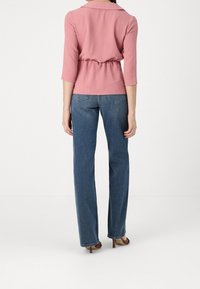 Helles pinkes Oberteil mit Kragen und Dreiviertelärmeln, tailliert, kombiniert mit geraden blauen Jeans und High Heels.