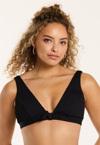 Melna trīsstūra formas bikini tops ar teksturētu audumu, platām siksnām un priekšējo mezglu. Iekšpusē ir gluda oderējuma apdare komfortam.