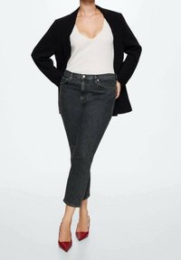 Černý blejzr přes bílý žebrovaný top, spárovaný s tmavými džíny a červenými lodičkami na vysokém podpatku. Čisté linie, přiléhavý silueta.