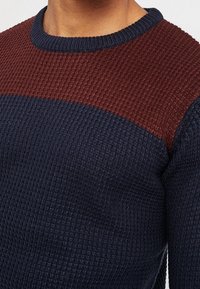 Stickad tröja med rund hals, med en vinröd övre del och mörkblå kropp. Texturerad tyg med ribbat mönster.