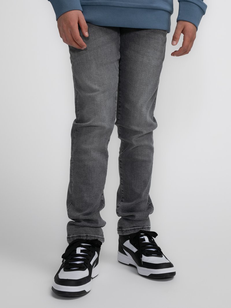Vaqueros de mezclilla gris con una textura suave, de corte ajustado, combinados con zapatillas negras y blancas con un diseño deportivo y cordones negros.