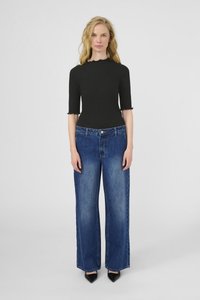 Melna ribota blūze ar zobainu apakšmalu, apvienota ar plaša kāju zilu džinsu biksēm ar izbalējušu apdari un smalku uzšuvumu. Melni norādīti zābaki.