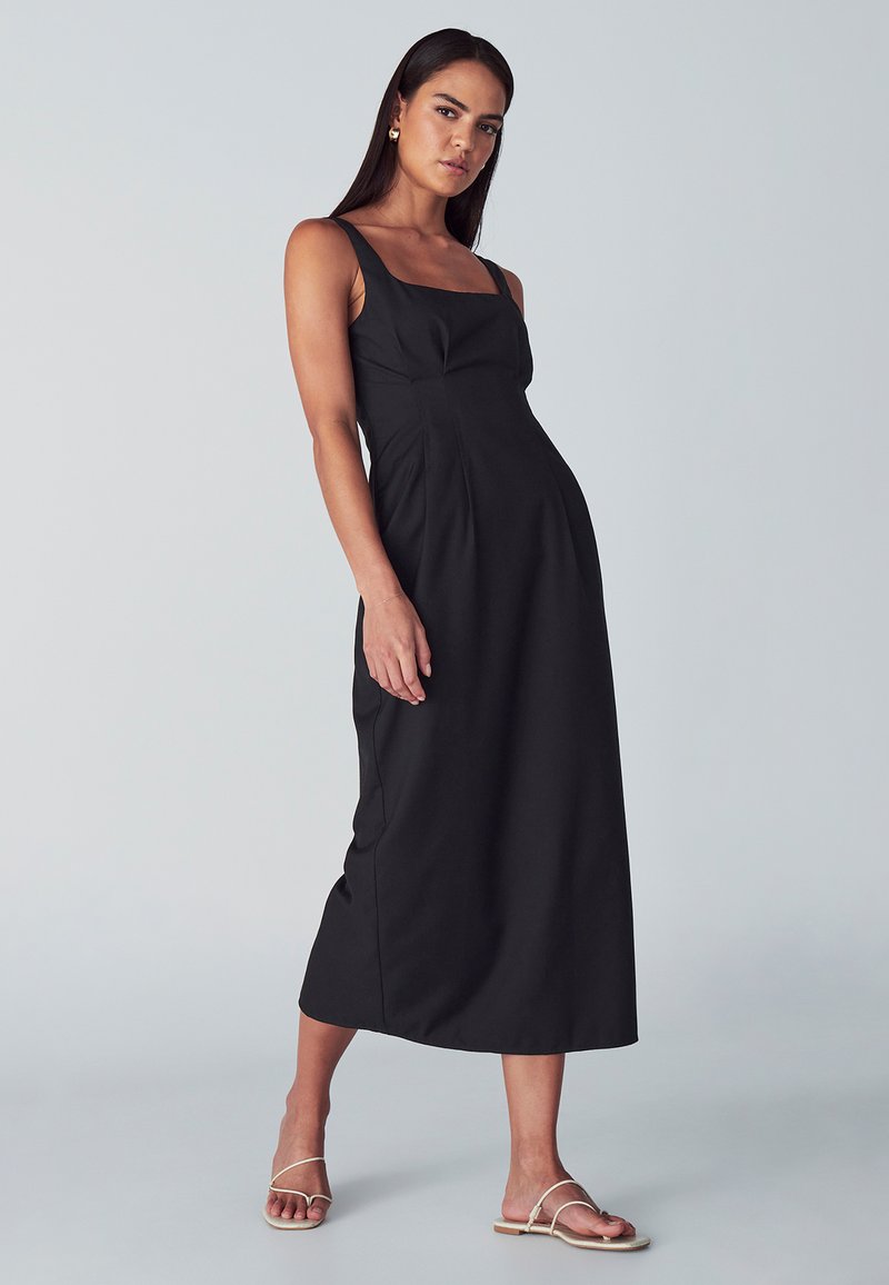 Črna brezrokavna midi obleka s kvadratnim izrezom, oblikovanim korpusom in tekočo krilo. Gladka tekstura s subtilnimi šivi.