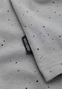 Tela gris con un patrón moteado en tonos negros y azules, con una etiqueta negra que muestra "ombre wear" cosida en el borde.