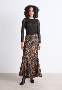 Top negro transparente de manga larga con patrón texturizado; falda maxi de estampado de leopardo en tonos amarillos y marrones; tacones negros de punta.