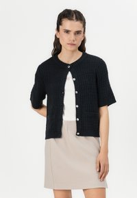 Marine gebreide cardigan met korte mouwen, een textuurpatroon, ronde halslijn en sluitingen met zilveren knopen, gecombineerd met een lichtbeige rok.