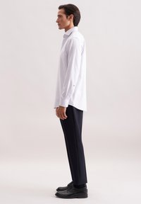 Camicia a maniche lunghe a righe bianche con polsini a bottone, abbinata a pantaloni dritti scuri e scarpe nere con lacci. Tessuto dalla superficie liscia.