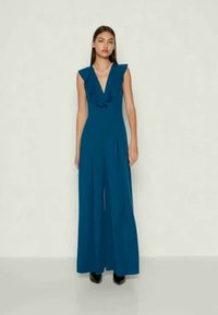 Telif jumpsuit z ruffled ovratom, brezrokaven dizajn in široke hlačnice. Gladka tekstura. Ukanjen z bisernim ovratnikom in črnimi čevlji.