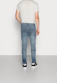 Ljusgrå t-shirt i kombination med ljusblå jeans med slim fit, detaljerad sömnad och fickor, kompletterat med svart-och-vita sneakers.