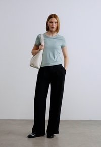 Ανοιχτό μπλε κοντομάνικο μπλουζάκι, μαύρο φαρδύ παντελόνι και μια κρεμ τσάντα ώμου. Το σκηνικό διαθέτει απλό ανοιχτό φόντο.