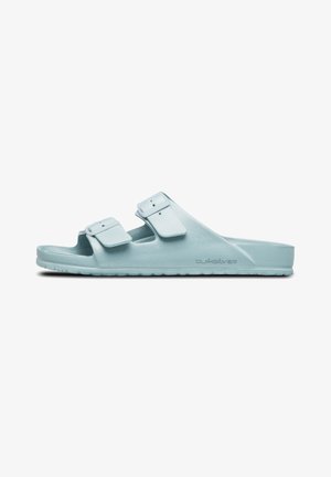 Light blue plastic slide sandals with two adjustable straps, flat sole, and textured footbed. Branding visible on the side.