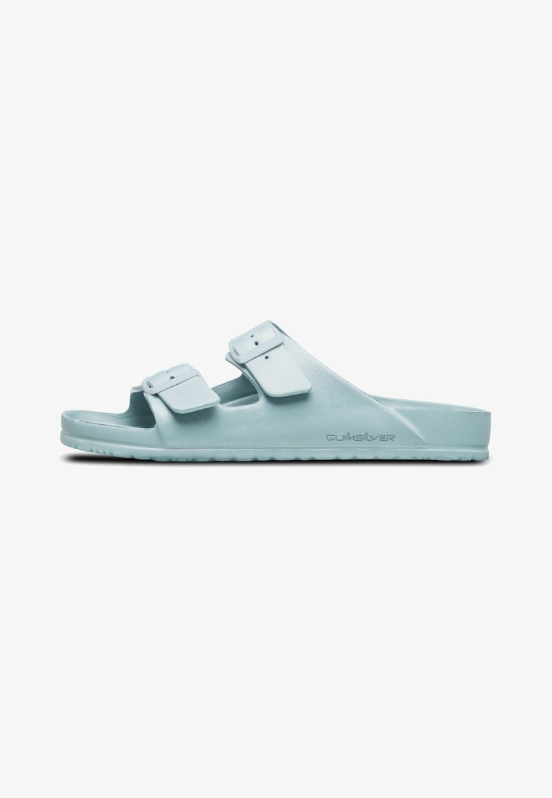 Light blue plastic slide sandals with two adjustable straps, flat sole, and textured footbed. Branding visible on the side.