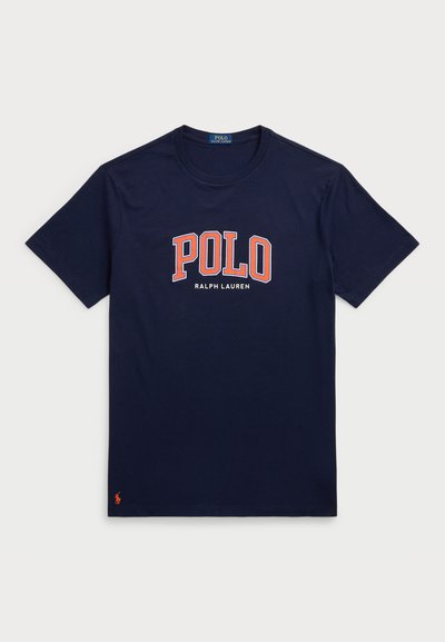 Tumši zili kokvilnas T-krekli ar īsām piedurknēm, ar lielu baltu un oranžu "POLO" logo un "RALPH LAUREN" tekstu zem tā.