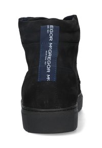 Zwarte suède enkellaars met een gestructureerde rubbere zool, voorzien van een blauw stoffen label met witte tekst op de achterkant. Eenvoudig ontwerp, geen extra accenten.