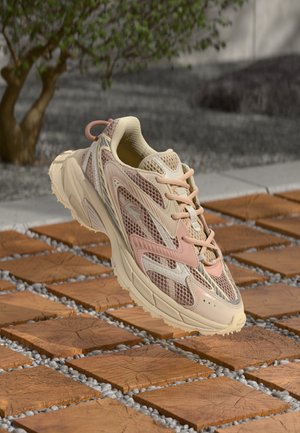 Sneaker featuring a mesh upper in cream and light pink hues, textured detailing, sturdy rubber sole, and contrasting accents.