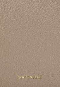 Světle růžová texturovaná kůže s jemnou zrnitostí, s pozlaceným embosovaným logem "COCCINELLE" na dně.