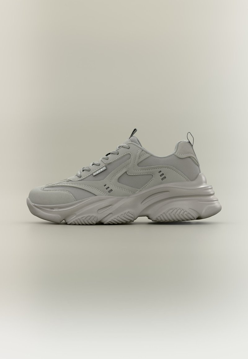 Χοντρό γκρι αθλητικό παπούτσι με ανάγλυφη σόλα, επάνω μέρος από πλέγμα και συνθετικό υλικό, κούμπωμα με κορδόνια και θηλιές στο γλώσσα και τη φτέρνα.