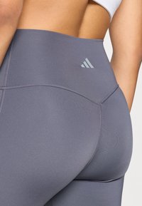 Leggings taille haute gris à texture lisse, avec un design cousu et un petit logo gris clair à l'arrière.