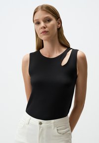 Top senza maniche nero realizzato in tessuto morbido, con scollo rotondo e un dettaglio distintivo a forma di apertura sulla spalla sinistra.