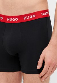 Čierne boxerky s červeným elastickým pásom so bielym logom "Hugo". Hladká látka s priliehavým strihom.