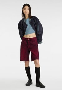 Námořnická bomber bunda, světle modrý crop top, červené džíny šortky s třepenými okraji, černé ponožky po kolena a černé slip-on boty se hroty.