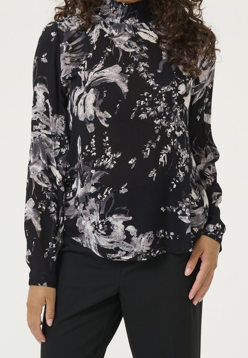 Blouse à manches longues en tissu noir avec des motifs floraux abstraits blancs et gris, dotée d'un col montant smocké et d'une coupe décontractée.